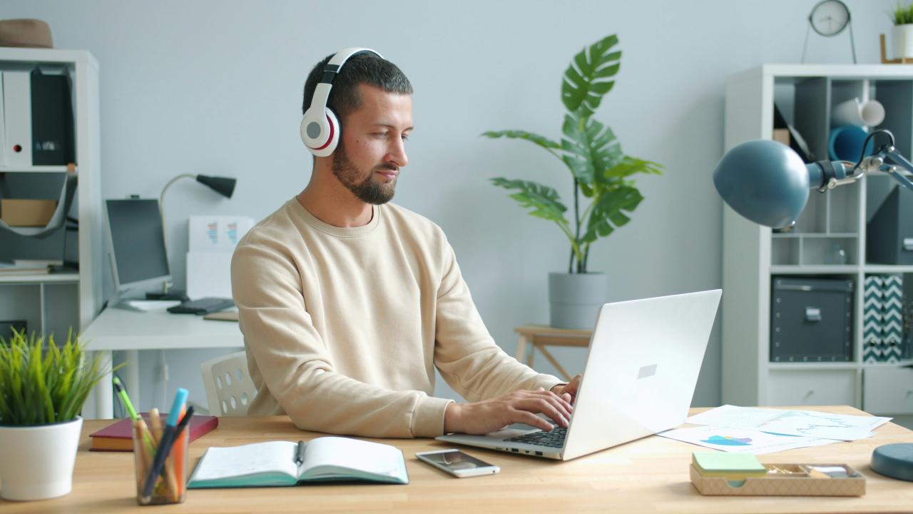 Pria yang mengenakan headphone bekerja di laptop di meja.